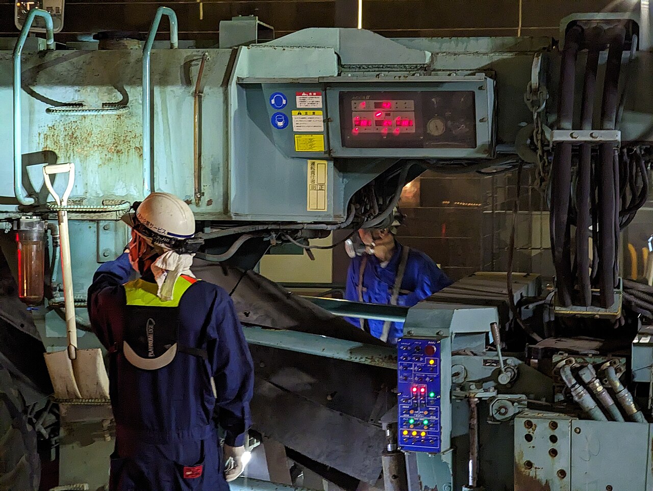 Two crew members checking the controls of a milling machine at night